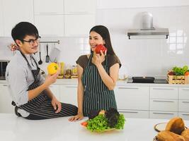 ásia casal preparando Comida dentro moderno cozinha segurando amarelo e vermelho pimento sorridente e Veja às a Câmera. foto