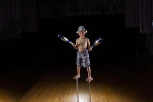 uma pequeno Garoto é uma circo artista em a cena malabarismo. circo crianças. executa criança acrobata. Treinamento uma pequeno malabarista foto