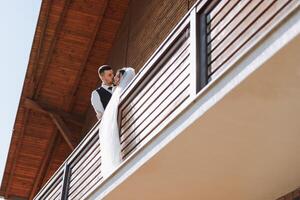 uma recentemente casado casal. a vento elevadores uma grandes branco véu dentro verão. a noiva e noivo estão abraçando, uma grandes véu é sopro dentro a vento. a recém-casados beijo em a sacada do a restaurante foto