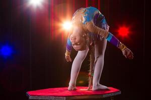 uma menina com uma flexível corpo. executa uma circo artista. circo ginasta. balanceamento agir. a criança executa a acrobático truque foto
