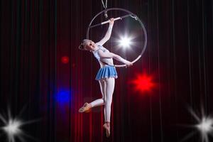 executa uma circo menina atriz. circo aéreo ginasta em a aro. acrobacia. adolescente executa a acrobático truque dentro a ar foto