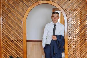 retrato do uma jovem noivo às casa antes a Casamento cerimônia. uma bonito homem vestido dentro uma clássico terno. masculino retrato. foto