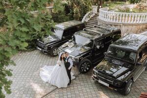 uma noiva dentro a elegante exuberante Casamento vestir e uma elegante noivo ficar de pé de seus Casamento carros. foto a partir de acima.