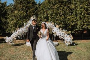 a noiva e noivo estão caminhando contra a fundo do a Casamento arco. ao ar livre Casamento cerimônia. noivo e noiva em a fundo do a Casamento arco. foto