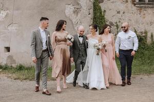 a noiva e noivo com seus amigos pose em a velho muro. uma lindo e elegante vestir do a noiva. à moda casamento. verão Casamento dentro natureza foto