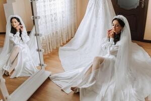 uma lindo noiva é sentado dentro uma vestir vestido dentro a manhã antes a Casamento cerimônia dentro uma hotel com uma moderno interior. incrível Penteado do a noiva. natural e moderno inventar. foto