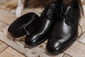 em a chão estão masculino Sombrio couro sapatos e uma Preto cinto, uma do homem terno em uma manequim, uma Casamento ramalhete do flores, Casamento argolas, masculino perfume. foto, topo visualizar. foto