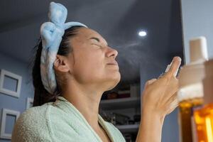 mulher aplica-se uma Vitamina spray para a pele do dela face. foto