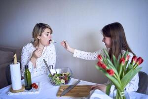 uma Adolescência menina e dela mãe dentro pijamas estão cozinhando e comendo uma fresco verde e tomate salada juntos foto