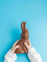 criança segurando chocolate Páscoa Coelho com orelhas mordido fora em azul fundo foto