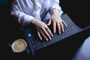 a idosos mulher trabalho dentro uma cafeteria às uma computador portátil foto