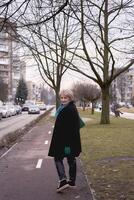 retrato do uma à moda velho mulher dentro uma Preto casaco com verde acessórios em uma Primavera rua foto