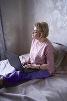 a idosos mulher trabalho com computador portátil às casa foto