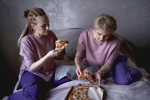 velho mãe e meia idade filha comendo pizza e assistindo uma filme às casa foto