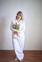 retrato do uma lindo tamanho médio mulher dentro pijamas com uma ramalhete do vermelho tulipas dentro uma minimalista estilo foto