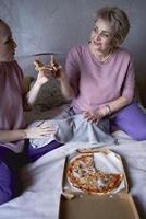 velho mãe e meia idade filha comendo pizza e assistindo uma filme às casa foto
