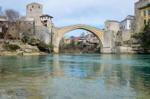 Visão do a velho ponte dentro Mostar cidade dentro Bósnia e herzegovina durante uma ensolarado dia. Neretva rio. unesco mundo herança local. pessoas caminhando sobre a ponte. foto