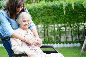 cuidador ajuda paciente idosa asiática com deficiência sentada na cadeira de rodas no parque, conceito médico. foto