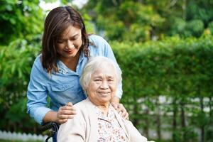 cuidador ajuda paciente idosa asiática com deficiência sentada na cadeira de rodas no parque, conceito médico. foto