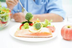 ásia idosos mulher paciente comendo salmão estaca e vegetal salada para saudável Comida dentro hospital. foto