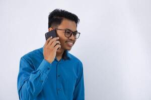 retrato do sorridente ou feliz bonito jovem ásia homem de negocios com óculos dentro vestindo azul camisa falando em Smartphone isolado em branco fundo foto