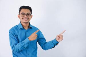 bonito ásia masculino empregado com óculos sorridente dentro uma pose dedo apontando para a lado vestindo azul camisa isolado em branco fundo foto