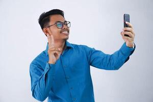 sorridente ou feliz ásia homem com óculos segurando Smartphone para selfie foto vestindo azul camisa isolado em branco fundo