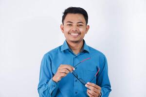 sorrir ásia homem segurando óculos e olhando Câmera vestindo azul camisa isolado foto