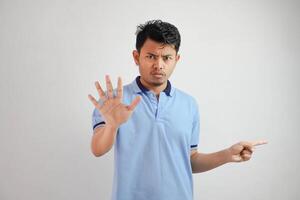 atraente ásia homem com mão gesto pose rejeição ou proibição enquanto apontando para cópia de espaço de dele lado vestindo azul t camisa isolado em branco fundo foto