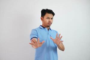 atraente ásia homem com mão gesto pose rejeição ou proibição enquanto apontando para cópia de espaço de dele frente vestindo azul t camisa isolado em branco fundo foto