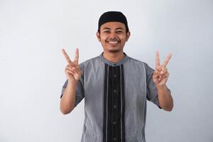 sorridente ou feliz jovem ásia muçulmano homem mostrando apontando acima com dedos número dois enquanto confiante e mostrando Paz placa com dedos vestindo Koko roupas isolado em branco fundo foto