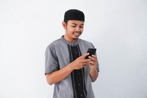 feliz ou sorridente jovem ásia muçulmano homem segurando telefone celular vestindo Koko roupas isolado em branco fundo. Ramadã conceito foto