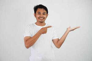 sorridente ásia homem com a aberto mão com dedos apontando para a lado vestindo branco t camisa isolado em branco fundo foto