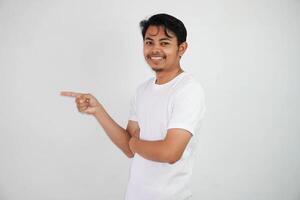 sorridente ásia homem com dedos apontando para a lado vestindo branco t camisa isolado em branco fundo foto