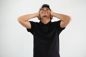 feliz jovem ásia homem ambos mãos segurando a orelhas e Veja acima vestindo Preto pólo t camisa isolado em branco fundo foto