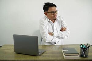 jovem ásia homem de negocios dentro uma local de trabalho fazer duvida gesto enquanto elevação a ombros vestem branco camisa com óculos isolado foto