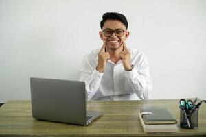 jovem ásia homem de negocios dentro uma local de trabalho sorridente com uma feliz e agradável expressão, vestindo branco camisa com óculos isolado foto