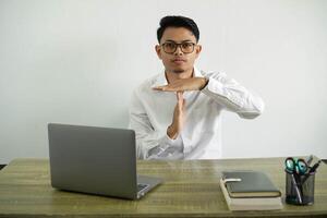 jovem ásia homem de negocios dentro uma local de trabalho fazer Tempo Fora gesto, vestindo branco camisa com óculos isolado foto