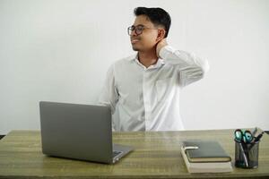 jovem ásia homem de negocios dentro uma local de trabalho segurando uma dolorido pescoço, vestindo branco camisa com óculos isolado foto