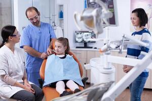 dental especialista falando com pai sobre criança boca hygine para saúde dentro dentista escritório. criança com dela mãe durante dentes Verifica acima com estomatologista sentado em cadeira. foto