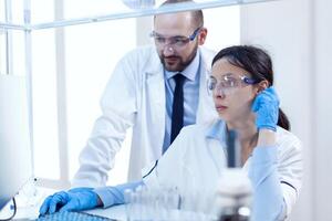 masculino cientista ajudando assistente com genético estude vestindo protetora engrenagem. equipe do pesquisadores fazendo farmacologia Engenharia dentro estéril laboratório para cuidados de saúde indústria. foto