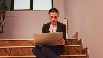 o negócio mulher excesso de trabalho com computador portátil sentado em escadas do o negócio Centro lendo financeiro relatórios enquanto colegas deixando escritório prédio. executivo Gerente fazendo hora extra às corporativo trabalho. foto