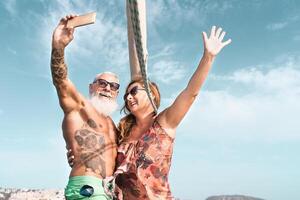 Senior casal levando selfie com Móvel Smartphone em barco a vela período de férias - feliz maduro pessoas tendo Diversão a comemorar Casamento aniversário em barco viagem - amor relação e viagem estilo de vida conceito foto