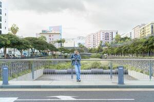 panorâmico Visão do raspada cabeça menina usando Móvel Smartphone enquanto ouvindo música com fones de ouvido dentro a cidade rua foto