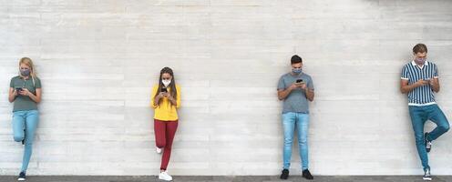 jovem pessoas vestindo cirúrgico mascarar usando Móvel telefone guardando social distância - milenar amigos assistindo meios de comunicação tendências em smartphones durante corona vírus surto - juventude e tecnologia conceito foto