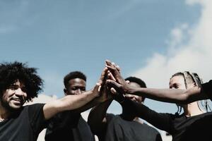 feliz grupo do africano pessoas tendo Diversão empilhamento mãos juntos ao ar livre foto