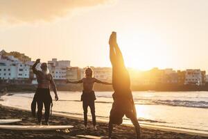 feliz em forma surfistas com diferente era e raça fazendo caloroso acima exercícios antes surfar durante pôr do sol Tempo - extremo esporte estilo de vida e amizade conceito foto