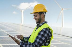 jovem engenheiro assistindo em digital tábua a Novo verde plano para alternativo energia com vento turbina e solar painel - inovação e verde poder conceito foto