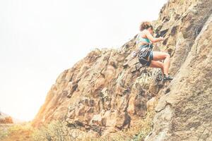 jovem mulher escalada em uma Rocha parede às pôr do sol - saudável alpinista realizando em Alto montanha - conceito do esporte, extremo, passatempo e estilo de vida foto