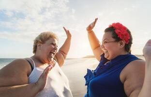 feliz excesso de peso mulheres tendo Diversão em tropical de praia durante pôr do sol Tempo foto